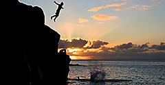 Boy Jumping off a cliff into the ocean at Waimea Bay. Hawaii