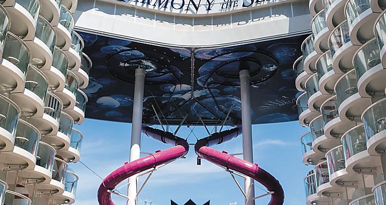 HM, Harmony of the Seas, Ultimate Abyss slide, day, daytime, long shot of purple tubes, people standing at end of slide on Boardwalk, waiting, ship signage and Crown & Anchor logo above, balconies on sides,