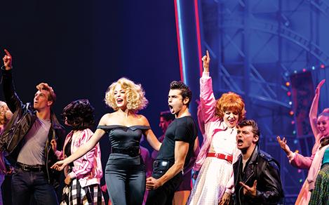 Performers singing and dancing on stage to the Grease Broadway show on Harmony.