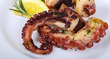 Grilled octopus on a white plate with a lemon on the side