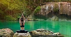 Woman practicing yoga on the rock in waterfall on the mountain