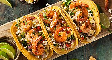 Three shrimp tacos with coleslaw and salsa on a wooden board