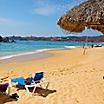 A tiki hut with a pair of tanning chairs out on the beach on Huatulco, Mexico