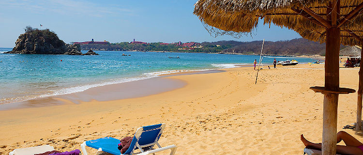 A tiki hut with a pair of tanning chairs out on the beach on Huatulco, Mexico