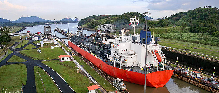 An industrial red ship entering the Panama Canal waterway that connects the Atlantic Ocean to the Pacific Ocean