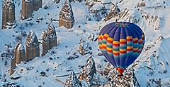 Hot air balloon riding tour flying over snow covered mountains of Cappadocia. Turkey.