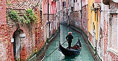 Gondolier punting gondola through green canal waters of Venice. Italy.