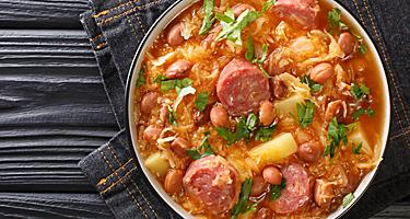 Jota Sauerkraut stew with borlotti beans, potatoes and sausages close-up in a bowl on the table. 