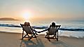 couple sitting in beach chairs on hold hands in front of a sunrise. The Caribbean.